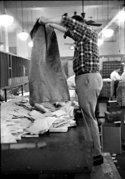 Postal worker, Eugene Hathaway, emptying a mail bag of letters onto a table for sorting crews at the United States Post Office on Monona Avenue. 