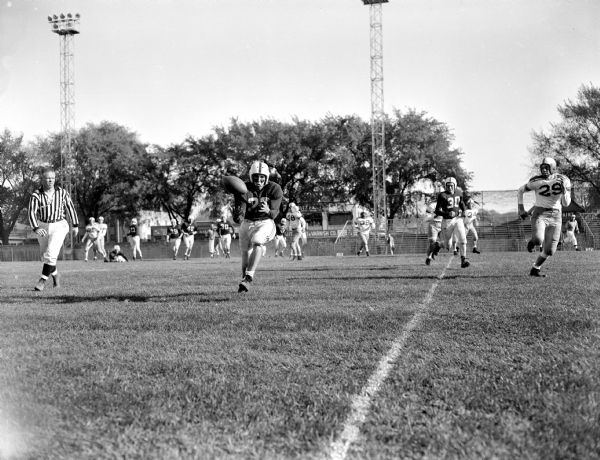 Football player catching a football, as the referee is officiating and defensive players are running up alongside the one handling the ball.