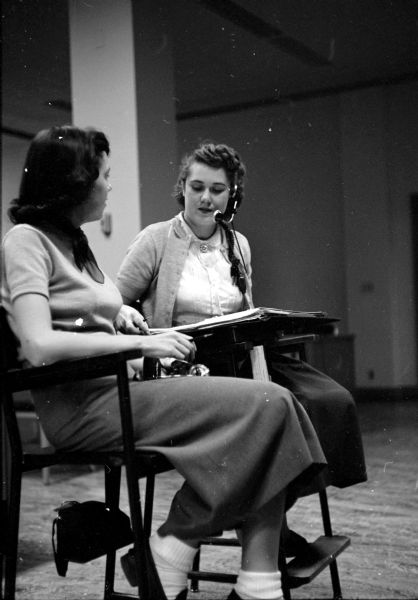 Operator Pat Stephenson (left) receives instruction from Mrs. Vivian Meicher, a supervisor at the Wisconsin Telephone Company, who is wearing a headset. The company employs about 250 operators, who work in several shifts. The women are casually dressed in light-weight sweaters, knee-length skirts, bobby socks and loafers.