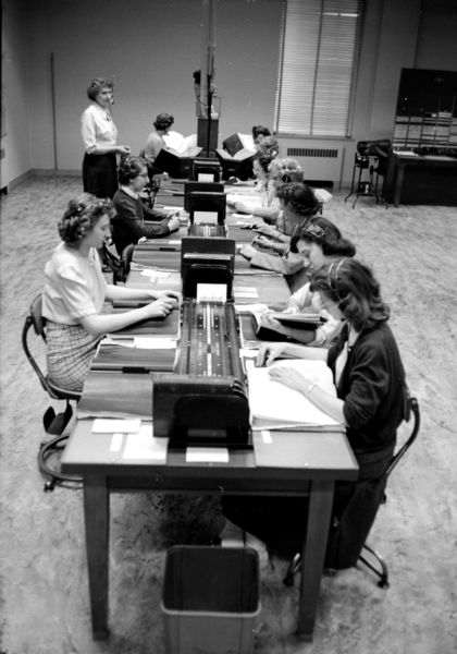 A group of people working at desks. One of these operators responds when someone dials for information. Most of their work is to provide telephone numbers of subscribers not listed in the directory.