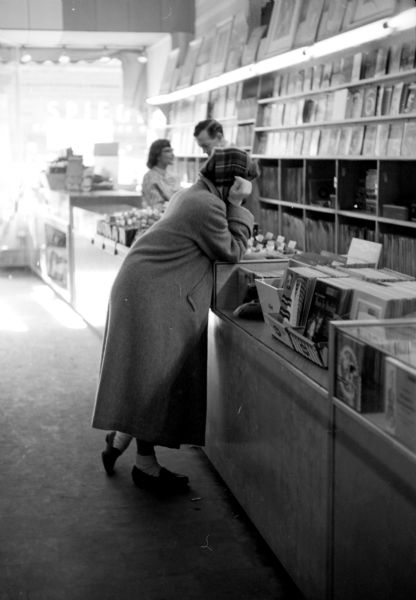 Customer Nancy Thomsen purchasing a vinyl record. Other 33rpm records are displayed along the back wall and counter top, and 45s are sitting inside a glass display case. Two sales people are in the background. 