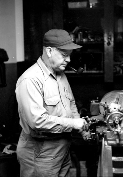 Captain Arne Lewick doubles as the fire station mechanic. Smoking a pipe, he is working at a lathe. 