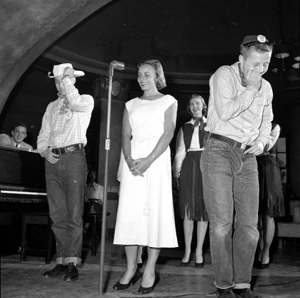 Prom queen candidate Jean Riley of Green Bay (a.k.a. "Calamity Jean") appearing with two "bashful cowhands," who are singing on her behalf at the rally in the Memorial Union Rathskellar. Clad in jeans, the performers are Dick Fjeldheim (left) and Pierre Slightam (right).