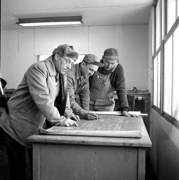Checking over blueprint plan details at the new Sears Roebuck store under construction on East Washington Avenue are Cy Perkins, George Lehmann, and Robert Olsen.