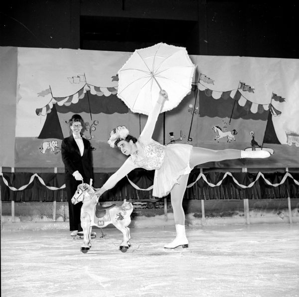 Members of the Madison Figure Skating Club held their annual winter party at the Truax Field Arena. The event was organized on a circus theme. Dorothy Mason is showing how to ride a pony on ice skates while holding an umbrella, as Ethel Lewis is watching from behind.