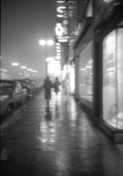 Pedestrians walking along State Street in freezing drizzle. Neon lighting and street lamps are illuminated and are reflecting off the icy sidewalks.