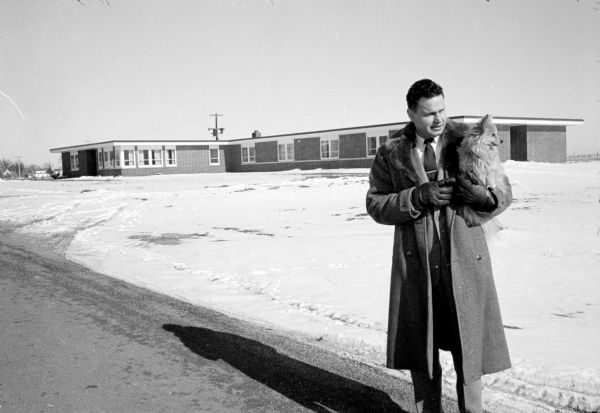 Winter scene of Dr. C.S. King, manager and part owner, standing in front of the Cuba City Hospital and Clinic. He is holding a small dog in his arms.