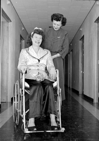 Two women from Illinois at the Cuba City Hospital and Clinic. One woman is pushing the other woman who is sitting in a wheelchair. 