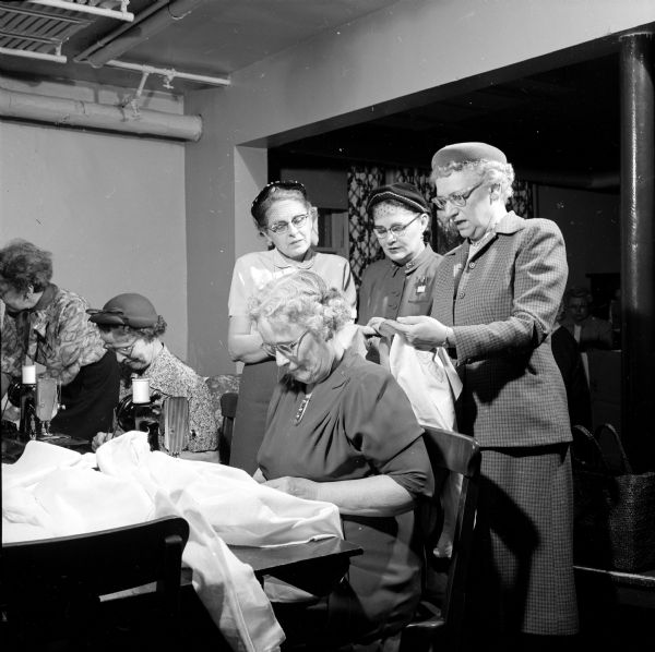 Members of the Methodist Hospital Service League during their monthly day of service sewing linens to be used in the hospital. Standing left to right are: Iola Reppen, Elizabeth Coulter, and Mrs. W.M. Harris. At the sewing machine is Clara Piper.  