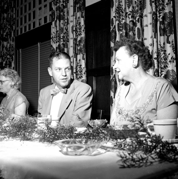 Members of the Capital City Chapter of the United Commercial Travelers Association attending a banquet at the Park Hotel. Sitting at the table are: John Grady and Mrs. George Limpert (from Appleton). There is a glass ashtray in front of them on the table by the decorations.