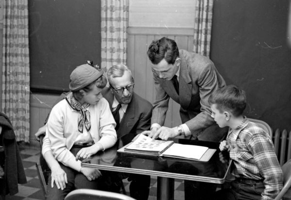 Arthur Schwebs, with his daughter, Karen, and son, Roger, are looking at a philatelic exhibit in an album at the Madison Stamp Club meeting at the City YMCA. Club president, Harvey Gifford, is looking on.