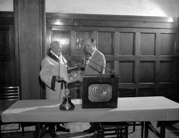 John Walsh, University of Wisconsin boxing coach, is showing an issue of <i>Esquire</i> magazine to General Olson at a Rotary Club meeting. The February issue featured an article written by Lou Sidran and was titled: "A Left Hook Is a Boy's Best Friend", on John Walsh.