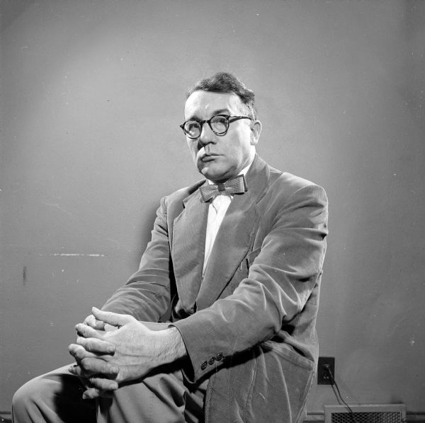 Portrait of Aldric Revell, sitting, political reporter for <i>The Capital Times</i> in 1954. He is wearing a suit and a bow tie.