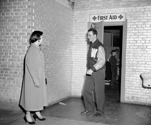 Connie Parnell (of Somerset, Wisconsin) meeting Bobby Meath of the University of Wisconsin boxing team at the door after his match. Meath is exiting a door that has a First Aid sign above it. He is wearing his Varsity Letter jacket.