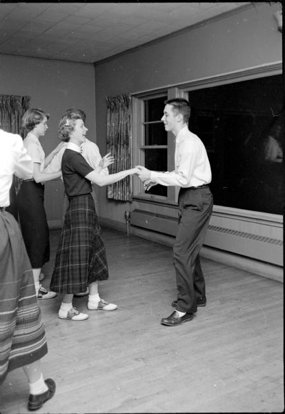 The Shorewood Hills Community League sponsored a dance class for teenagers at the Blackhawk Country Club that was taught by Arthur Murray instructors. Ailene Peterson, wearing saddle horn shoes, and Bob Coleman are shown learning a step amidst other couples.
