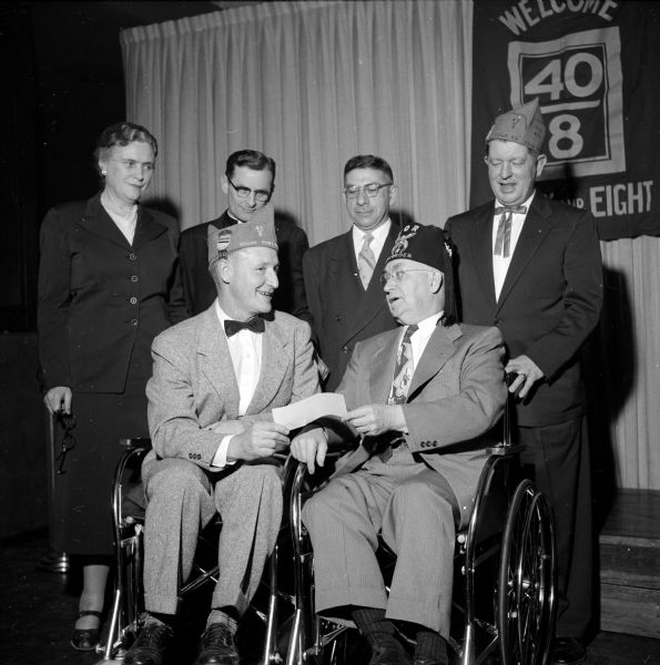 At the Annual Dane County American Legion 40-and-8 banquet, they collected money for local charities. In the photograph R.C. Golden hands a check to Clyde Wilson of Zor Shrine. Standing in back are Lucile B. Graves (public health nurse), Reverend E.J. Van Handel (Catholic Welfare Bureau), Rabbi Manfred Swarzensky (Jewish Welfare), and Randall Rogers (county chef de gare). The title for this legion group comes from box cars used  during World War I to transport troops to the front line in France: They would carry forty men or eight horses.