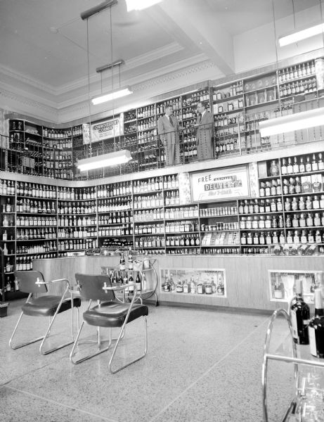 Liquor store at the Park Hotel. Two men are standing on the upper level of the two-story display of bottles, which is well lit.