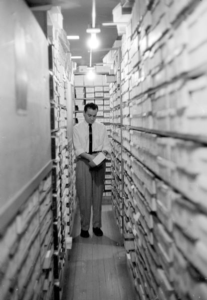 Shoe salesman, Larry Borenstein, standing in a narrow aisle of the shoe stockroom at Borenstein's Dry Goods Store located at 1980-81 Atwood Avenue.