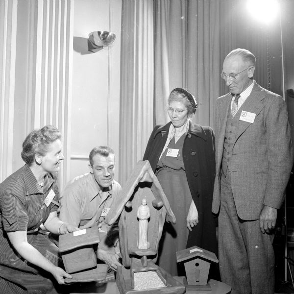 Mr. and Mrs. F.B. Mayer of Two Rivers are discussing bird house construction with Mr. and Mrs. Henry Koenig of Sauk City. They are standing on either side of a bird house depicting St. Francis of Assisi inside a niche.