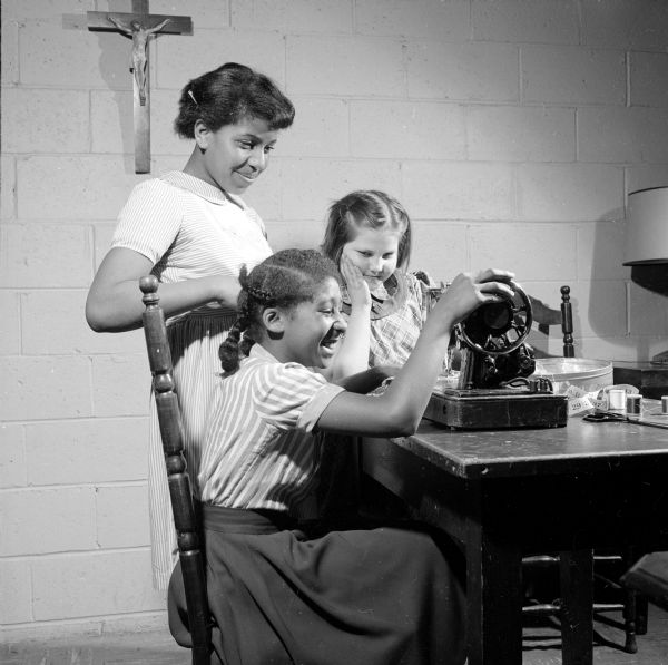 Maria Johnson and Patty Poppa are looking on as Donna Harris is adjusting a sewing machine at Blessed Martin House. The girls in the sewing class made dresses for dolls to be sent to an orphanage in Japan.