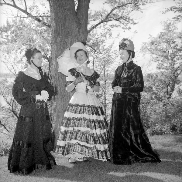 Three women attending the Republican Centinnial Birthday party are shown in period fashions in the style show associated with the celebration. Shown left to right are: Mrs. L.A. Dougherty, in a late 19th-century gown; Mrs. Page Johnson, in a dress of 1854 and holding an umbrella; and Mrs. John Walsh, representing 1872.