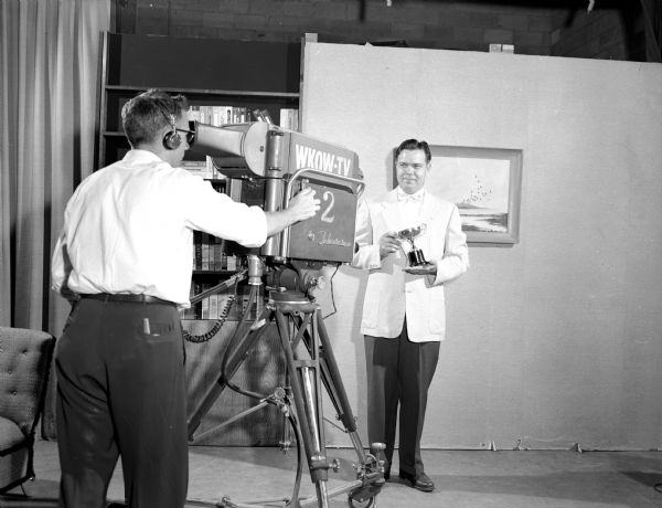 Presentation of the Master Television Engineer award to Cloren Smith, Chief Engineer at WKOW-TV in Madison. Smith is seen holding a mounted cup on a studio set as he is being recorded by a cameraman for WKOW-TV Channel 2.