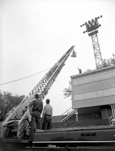 Firemen practice demonstrating the rescue of people from a burning building with an aerial ladder. They are preparing for the Police and Fireman's show at Breese Stevens Field. Proceeds from the show went to three charity organizations.