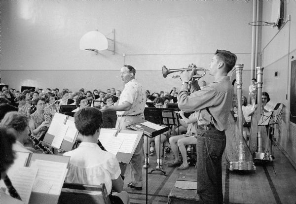 George Houslander, Director of the Royal Canadian Air Force Band, leading a band practice session in a gymnasium at the University of Wisconsin Music Clinic. The trumpet soloist is Roger Bloemers from Oostburg.