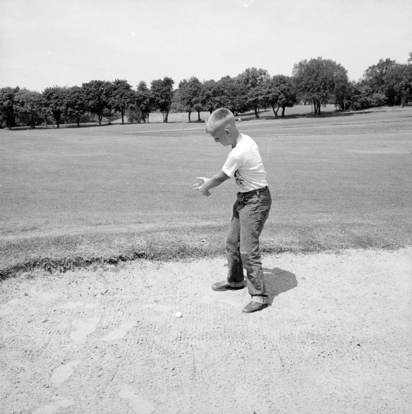 Photograph of Brad Walrath to make a composite image that was published in the newspaper of him holding an enlarged golf club in a sand trap at Maple Bluff Golf Course, with quote: "I can keep my head up, but I don't know how much longer I can keep the club up."