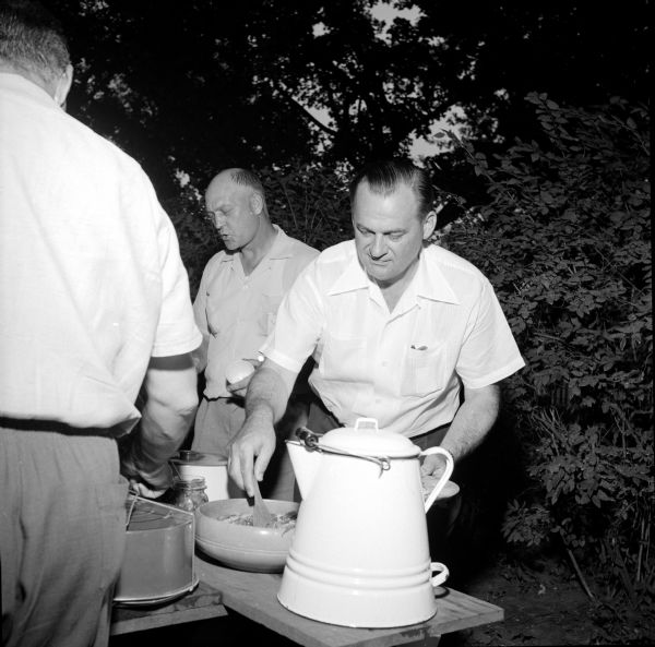 Alderman George Reger and Mayor George Forster (right) loading up their plates at the outing. Mayor Foster is dishing up food that is sitting behind an enameled white kettle at the end of the picnic table.