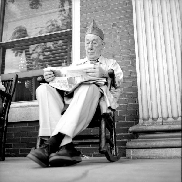 B.A. Clark shown taking time out for relaxation on the porch of the Elks Club, headquarters for the Wisconsin American Legion's 40 and 8 Grande Promenade. He is sitting in a rocking chair.