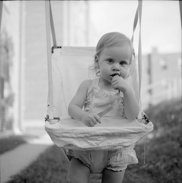 Laurie Stein (the photographer's daughter) in a bouncy swing. She is chewing on wooden clothes pins.
