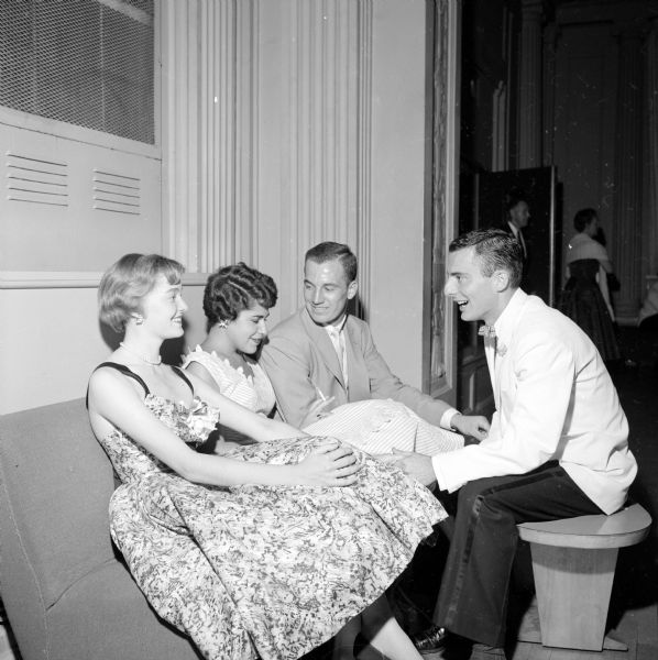 Two couples take a break from dancing to chat in a corner at the university summer prom at the Memorial Union. From left to right are: Canole Schlich (of Nashville, Tennessee); Ann Plummer (from Milwaukee); Alan Anderson (from Chicago); and Richard Thomar (of Madison). Ann is holding a cigarette between her fingers.