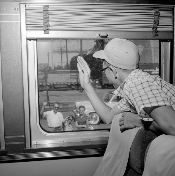 Madison Newspapers, Inc. newsboy, Fred Ciebell (from Edgerton) waving goodbye from a window to his parents, Wes and Elaine Ciebell, and brother. Fred is inside the train before a week-long trip in the nation's capitol.
