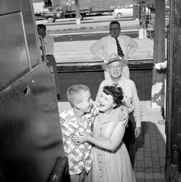 Madison Newspapers Inc. newsboy John Pertzborn gives his mother, Margaret Pertzborn, a goodbye hug before boarding the train for a week in the nation's capitol. Looking on is John's grandfather, E.D. Jones. The unknown man standing on the platform in the background with a cigarette in his mouth was cropped out of the image when it was printed in the newspaper.