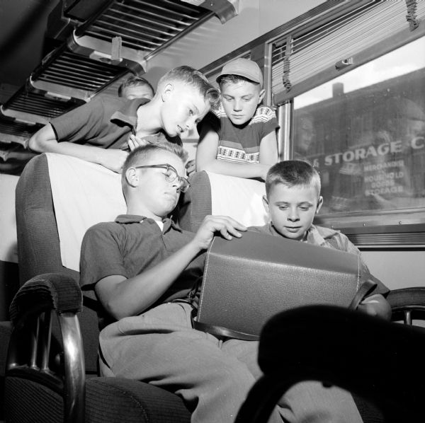 Sitting on the train and ready for a trip to the nation's capitol are Madison Newspapers, Inc. newsboys, Gerald Schroeder (left) and Billy Adelman (both of Reedsburg). Standing in back are David Pernot and Phil Synder (both from Brooklyn). They are looking at a bag on on their laps.