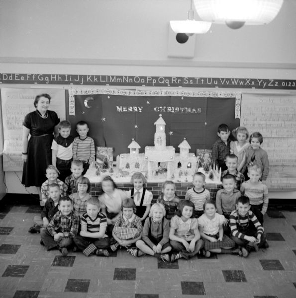 Shorewood Hills first-grade teacher, Dorothy Sliter, posing with her twenty-three pupils by a model of Santa Claus' castle, which they made for presentation to the children's ward of Madison General Hospital. 