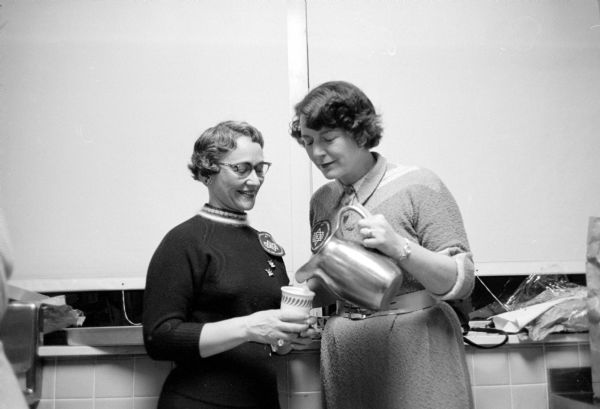 Elizabeth Woods holding the cup while Judith Stein is pouring coffee at the holiday party for patients at the Veterans Hospital. The women's division of the Madison Jewish Welfare Board is one of the groups which make up the VA hospital voluntary service committee.