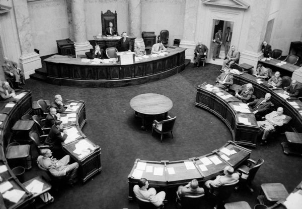Elevated view of members of the 1955 Wisconsin State Legislature Senate listening as Chief Clerk Lawrence Larsen (standing)is reading the next order of business.