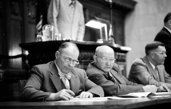 Former State Assemblymen Herman Eisner of Cross Plains (left) and Harry Holmes of Landcaster (right) serving as journal clerks to "keep the books" for the 1955 State Assembly. The two men on the far right are unidentified.