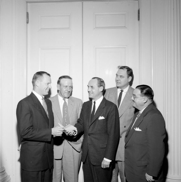 Norbert Mayer (far left) is presenting an invitation to Governor Walter Kohler (center) to attend a "Man of the Year" testimonial dinner for Gavin McKerrow, president of the Golden Guernsey Dairy Co-op. The dinner is sponsored by the Pewaukee Chamber of Commerce.  Also pictured are: William Shell (between Mayer and Kohler) and to Kohler's right are Roland Aldrich and Roy Bernier. All (except Kohler) are members of the Pewaukee Chamber of Commerce.