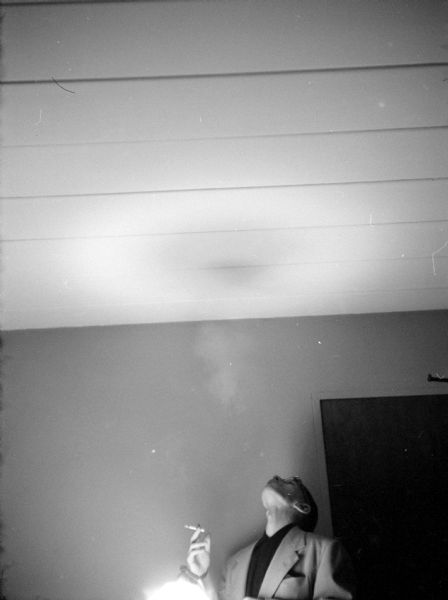 Man smoking a cigarette and blowing a smoke ring towards the ceiling.