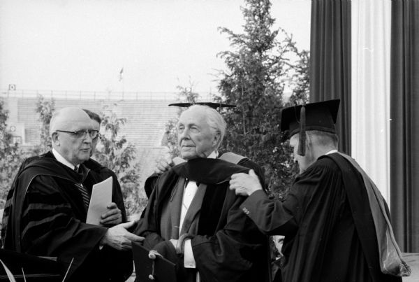 Professor Ben Elliot placing the doctoral hood on Frank Lloyd Wright at the University of Wisconsin Commencement ceremony. U.W. President Edwin Broun Fred is on the left.