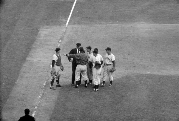 During the 5th inning of the Milwaukee Braves vs. the Cincinnati Redlegs game, Redlegs manager, Birdie Tebbetts (wearing a jacket), argues with the umpire, Hal Dixon. Braves catcher, Del Crandall, and several Redlegs players are standing by.  