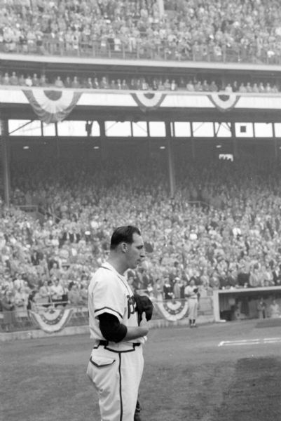 Pitcher Warren Spahn bows his head as the fans in Milwaukee County Stadium pause during the pre-game ceremonies for a minute of silent tribute to the late Fred Miller.