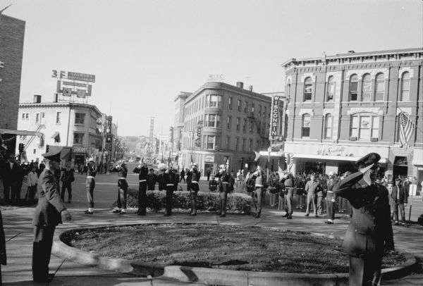 Soldiers fire 21-gun salute during Veteran's Day ceremony held at the State Street entrance to the State Capitol. Businesses seen in the background left to right are: Sandra Hat Shop at 101 State Street (with 3F Laundry sign); Commercial State Bank, 102 State Street; and Wisconsin Life Insurance, 26-30 West Mifflin Street.        