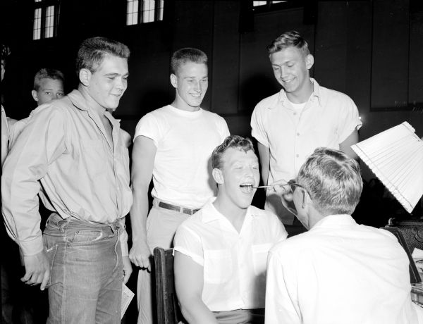 Dr. Donald Simley examines the teeth and tongue of Jon Rockstad as three other returning lettermen look on. In the back row are John Davidson, John Hill and Dale Hackbart.  