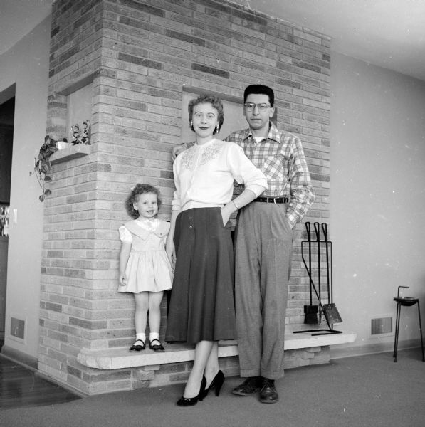 A couple with their young daughter posing in front of a home fireplace to take a photograph for their Christmas Card.