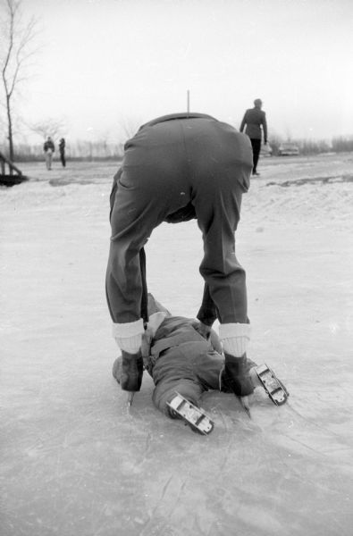 Francis Nerlinger helping daughter, Susan Jane, after she fell face forward on the ice at Vilas Park ice rink by Lake Wingra.
