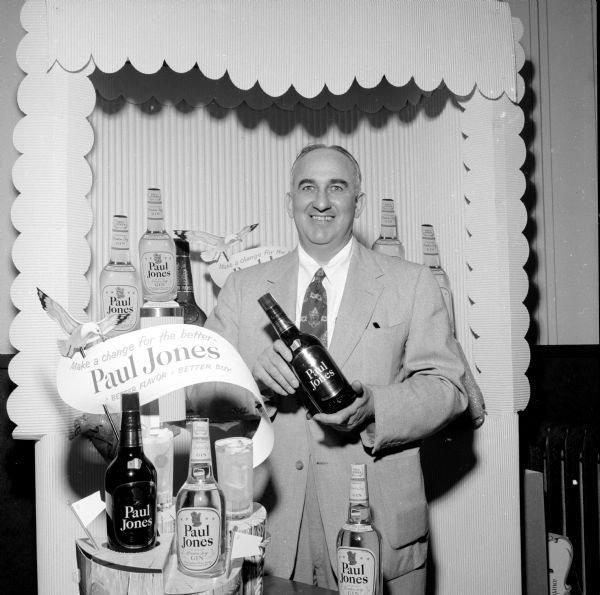 Hy Novis (?) holding a bottle by a Paul Jones liquor display.